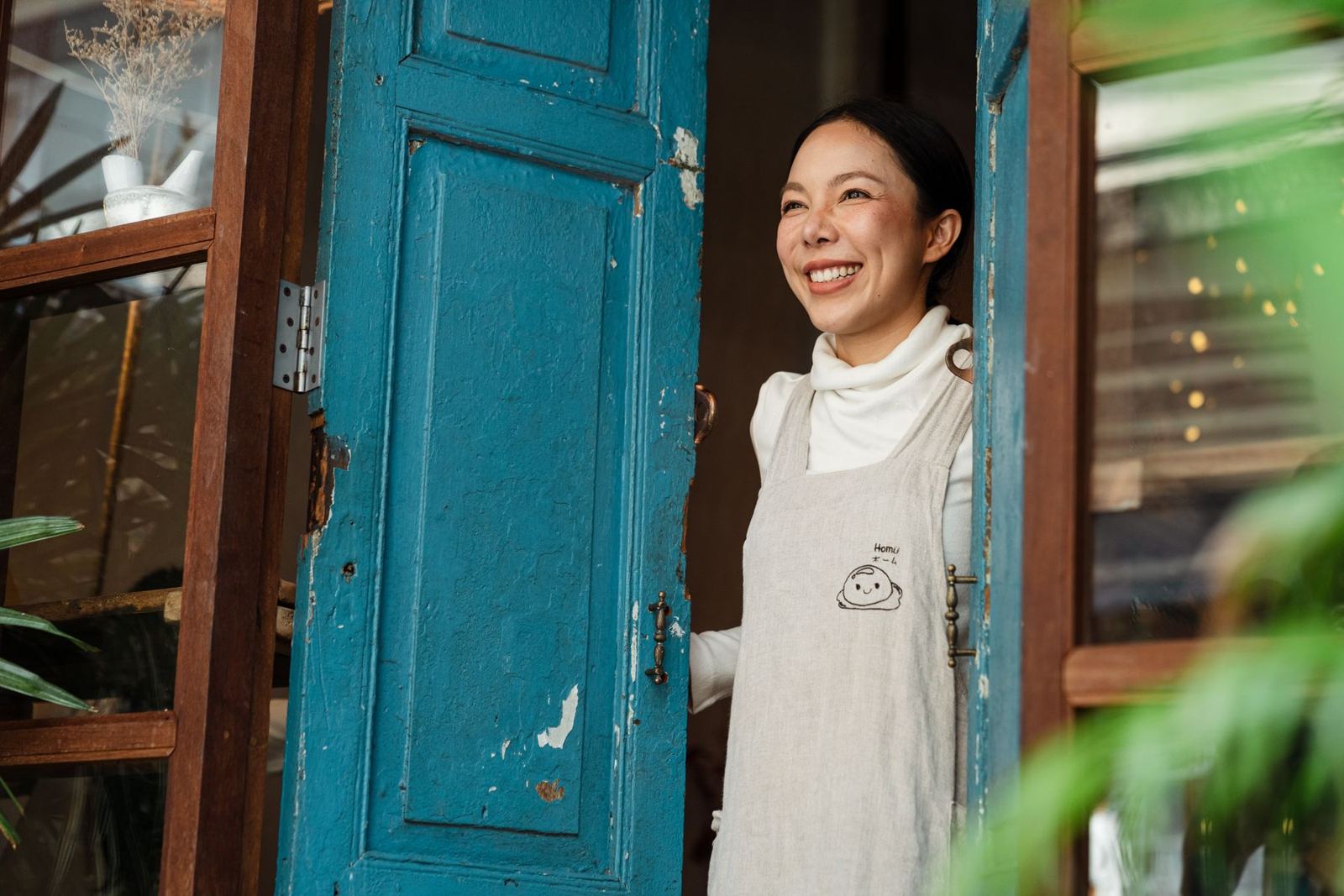 A smiling cafe owner standing at the open door of her cafe