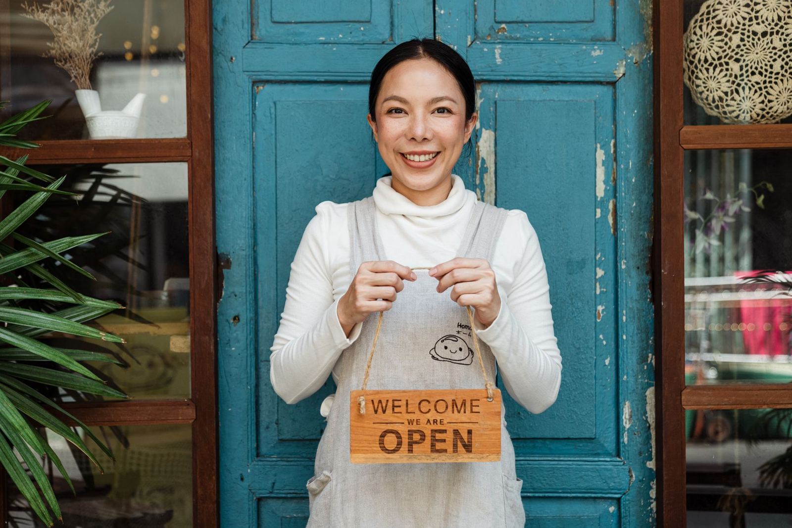 A cafe owner at her front door holding a sign that says welcome, we are open